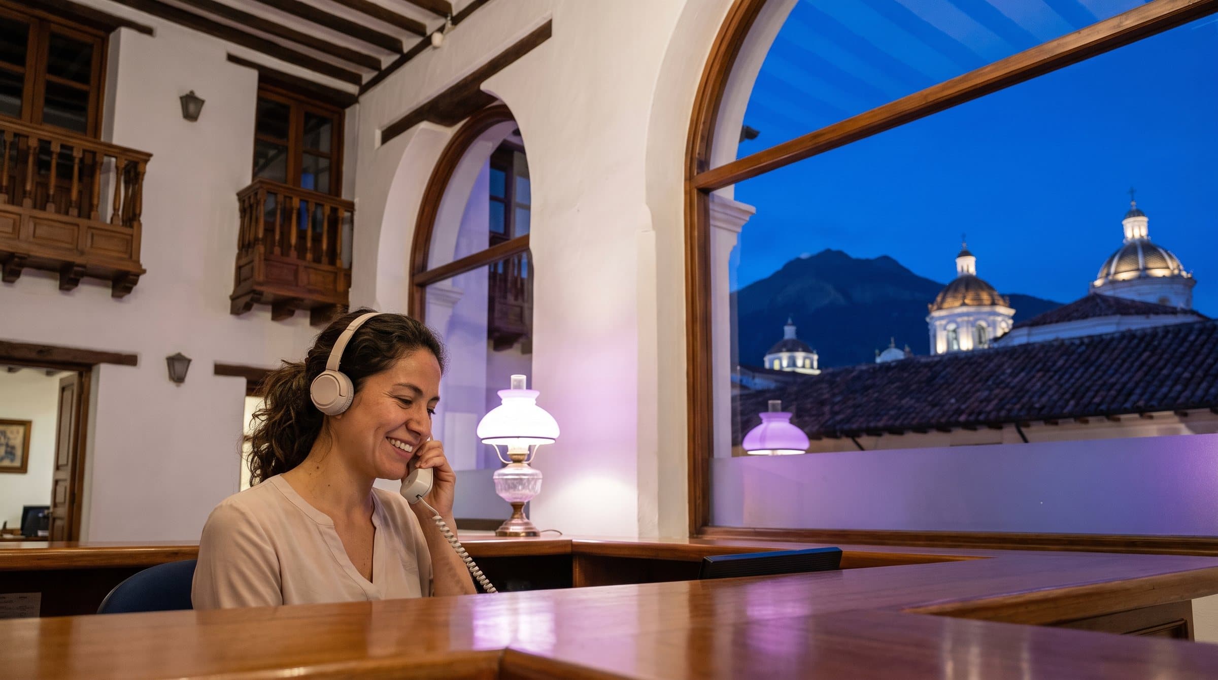 Recepcionista con diadema contestando el teléfono en una clínica de un edificio colonial del centro histórico de Quito, con el Pichincha al fondo
