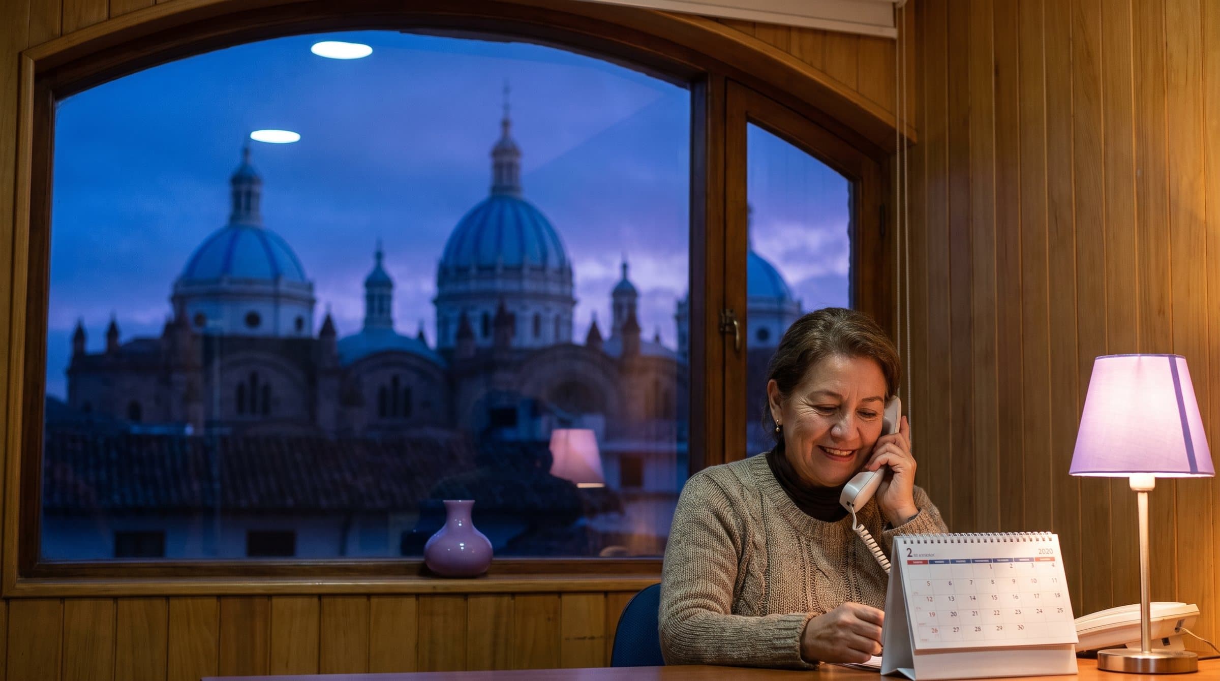 Recepcionista de un consultorio dental en Cuenca al teléfono, con las cúpulas azules de la catedral al amanecer